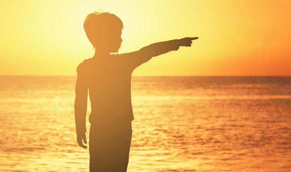contour of a boy at sunrise sunset on the seashore of the ocean orange sky sea ocean boy shows his finger to the side. High quality photo