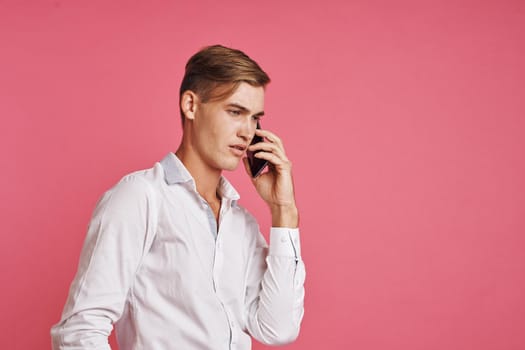 handsome man in a white shirt talking on the phone pink background. High quality photo
