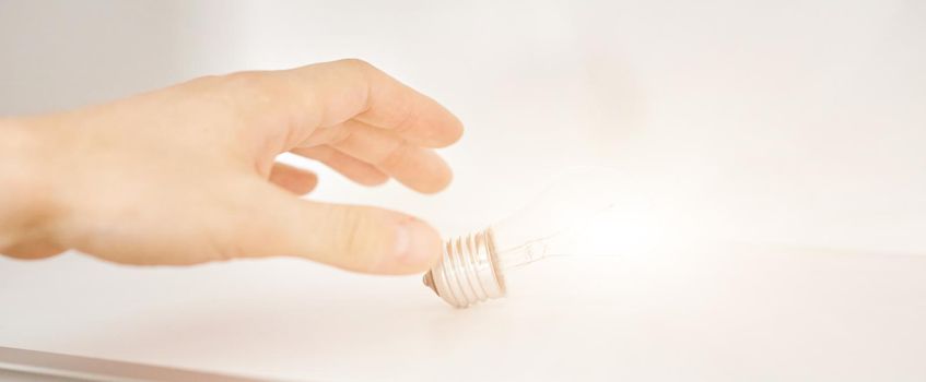 hand reaches for a glowing light bulb on a white shelf. The concept of aspiration behind the idea . High quality photo