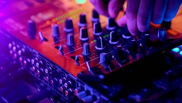 Hands of DJ mixing tracks on professional sound mixer..Closeup,knobs and regulators in focus. High quality photo