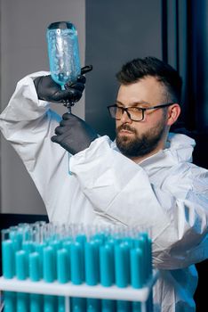 A man Scientist in a protective suit with flasks in his hands with a blue vaccine