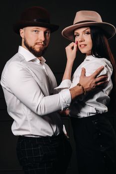 A man and a woman in white shirts and hats on a black background.A couple in love poses in the interior of the studio.
