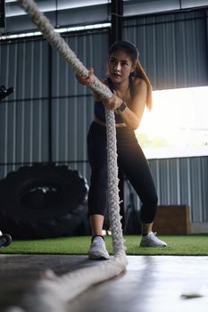 Female working out with battling rope at gym. Healthy modern people concept.