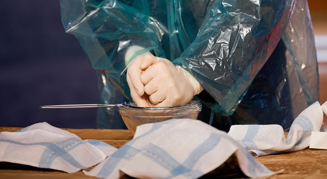 a man in a protective cloak with his gloves presses the juice into a glass plate. High quality photo