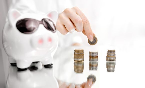 woman on a mirrored table collects coins near the piggy bank. High quality photo