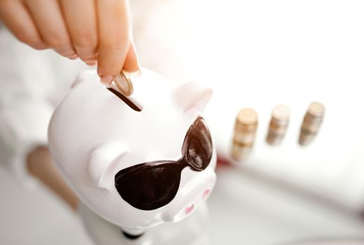 women's hand fills piggy bank from stacks of coins standing next to . High quality photo