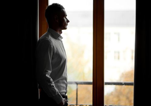 guy in a white shirt looks at the city through the window. High quality photo