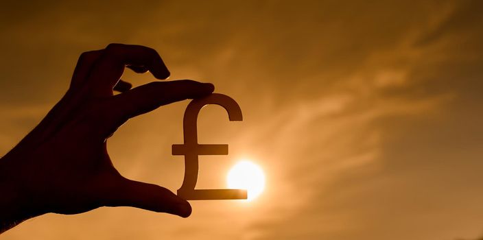 The symbol of the pound sterling in the hand contoured at sunset . High quality photo