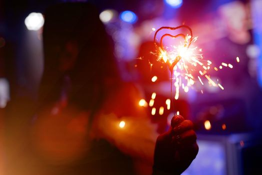 Girl holding burning sparkler in heart shape. High quality photo