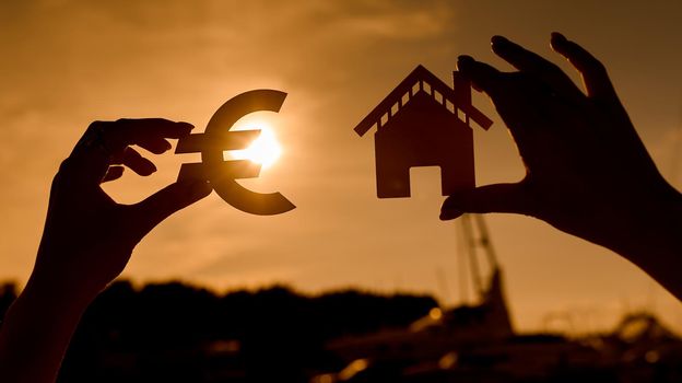 Euro symbol and house in women's hands contoured at sunset. High quality photo
