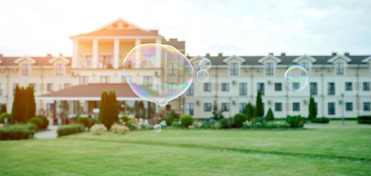 beautiful soap bubbles fly in front of a blurry respectable house with a park . High quality photo