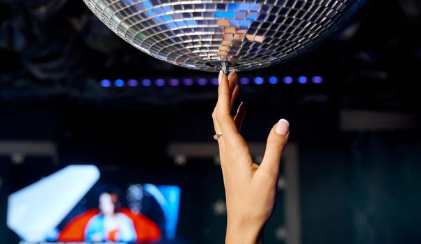 Beautiful female hand reaches for the disco ball and swings it. High quality photo