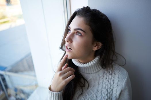 brunette in a white sweater looks out the window depression. High quality photo