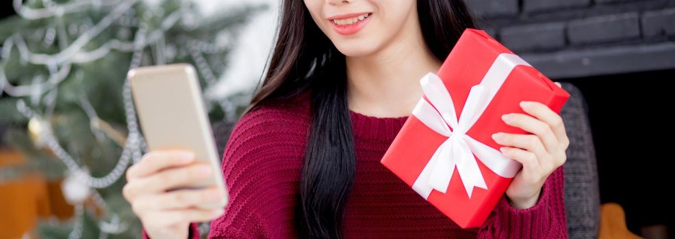 Young asian woman selfie video call online with friends and show gift box in Christmas day on phone at home, social distancing, new normal, female video conference, communication and holiday concept.