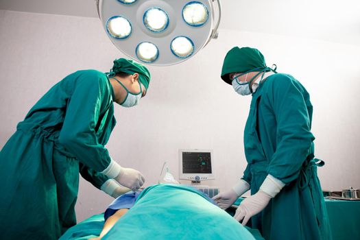 Team doctor and assistant holding oxygen mask with patient emergency in the operation room at hospital, surgeon healing and surgery, problem of breathing, instruments medical and health.