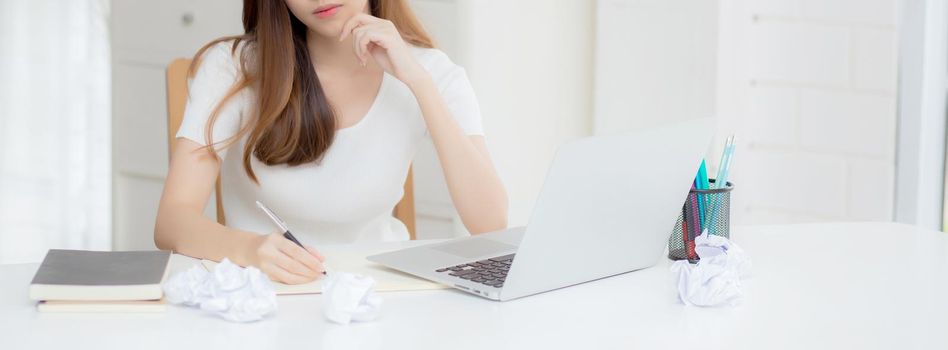 Young asian woman working with laptop computer think idea project and paper crumpled having problem on table at home, girl using notebook with frustrated and trouble, business and freelance concept.