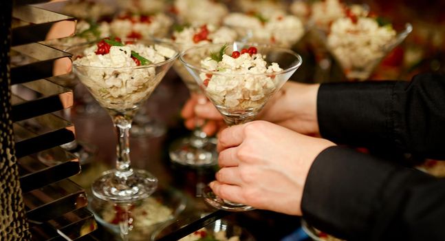 Waiter puts on a glass shelf salad with mayonnaise in glasses for Martini . High quality photo