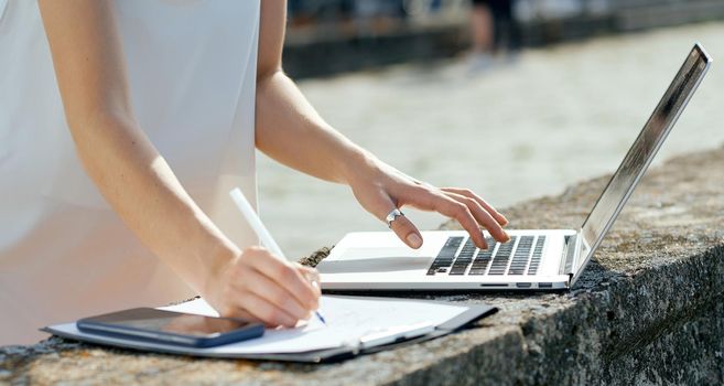 beautiful, serious girl in a white dress with a tablet, pen, laptop phone on the dock. High quality photo