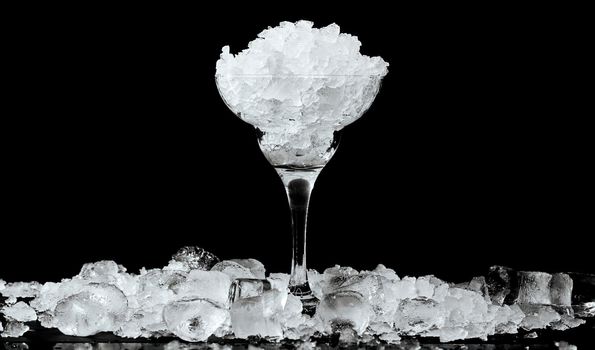 Cocktail glass with ice inside and scattered outside on a black glossy background. High quality photo