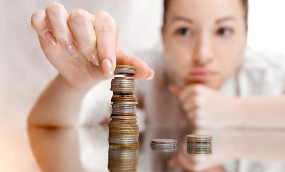 A thoughtful woman shifts coins from the pile to the pile. There's a coin tower. . High quality photo