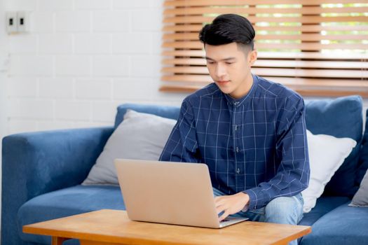 Young asian man typing keyboard on laptop computer on desk at home, businessman working to internet online, freelance male using notebook on table, communication and lifestyle concept.