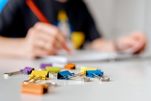 Multi-colored paper clips are scattered in the foreground. In the background, a man writes. High quality photo