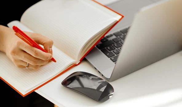 woman records red pen in notepad next to laptop . High quality photo
