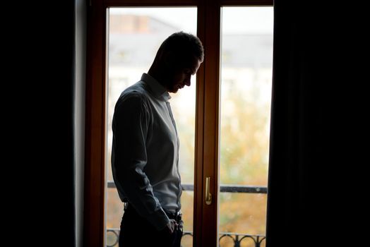 sad guy in a white shirt with a short presy standing at the window. High quality photo