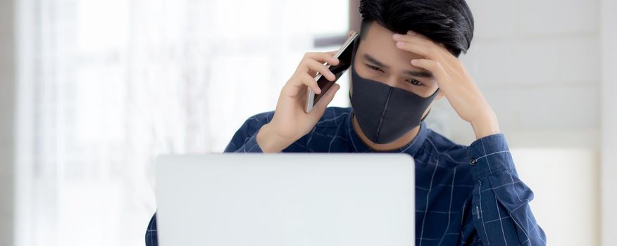 Young asian business man in face mask talking smartphone and work on laptop computer for protect covid-19, businessman quarantine work from home with notebook, social distancing and stay home.