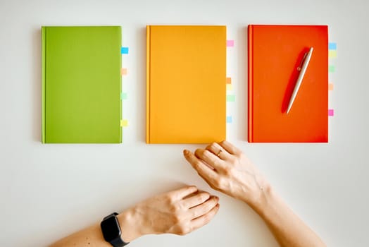 Woman try to choose green yellow red notebooks on white table. High quality photo