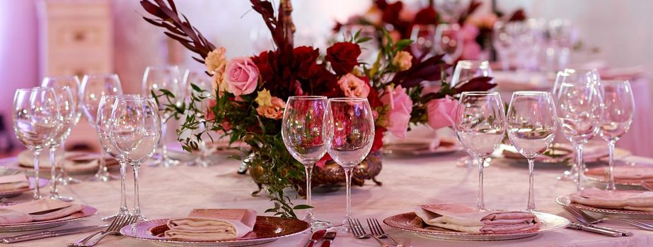 A dining table filled with wine glasses served for guests. Table with flowers in the middle. High quality photo