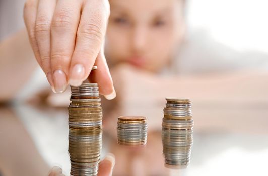 A blurnt woman in the background, a sharp hand in the foreground on a mirrored table collects stacks of coins. High quality photo