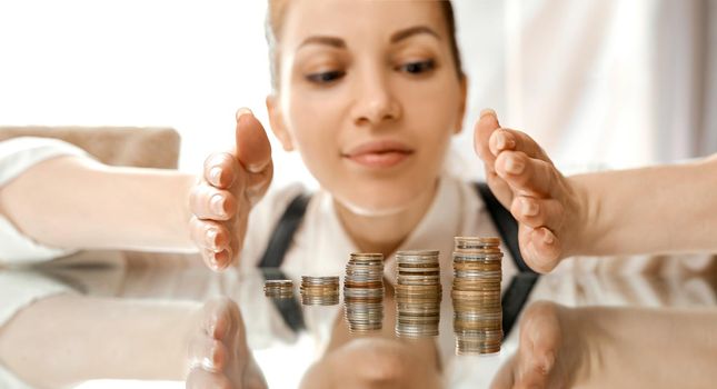 A woman covers saves money stacks of coin table. Look with savings . High quality photo