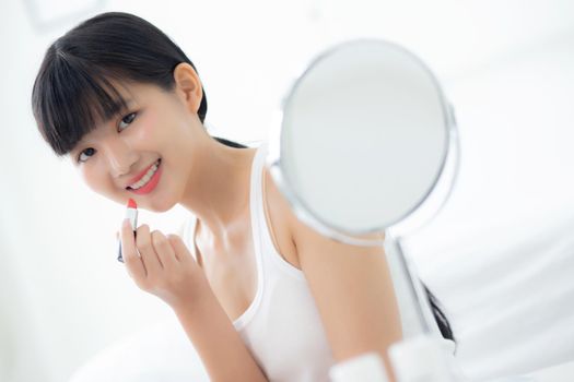Beautiful young asian woman applying lipstick red on mouth, beauty girl looking facial at mirror for makeup cosmetic with lips elegance, make up with sexy of female, skin care and health concept.