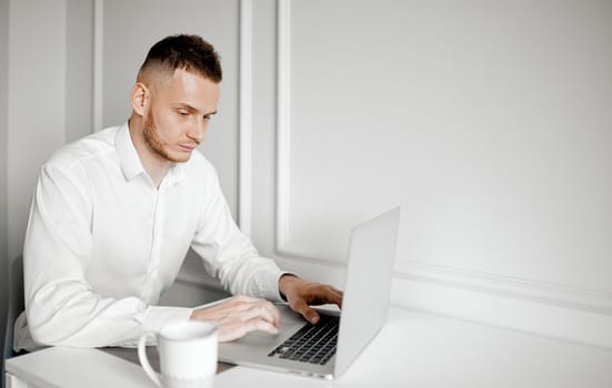 A young businessman works at a table with a cup of coffee and a laptop. High quality photo