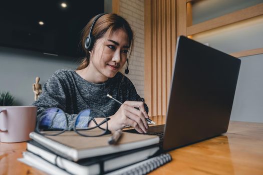 Happy asian woman in wearing headphones, enjoying watching educational webinar on laptop.