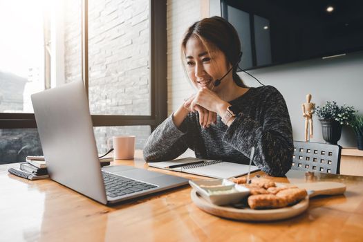 Happy asian woman in wearing headphones, enjoying watching educational webinar on laptop.