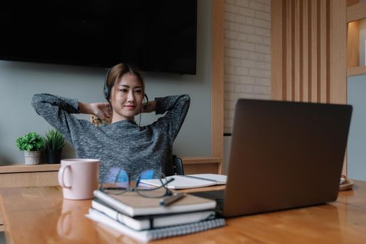 Happy asian woman in wearing headphones, enjoying watching educational webinar on laptop.