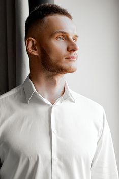 young man in white shirt stares to the left side of the window. High quality photo