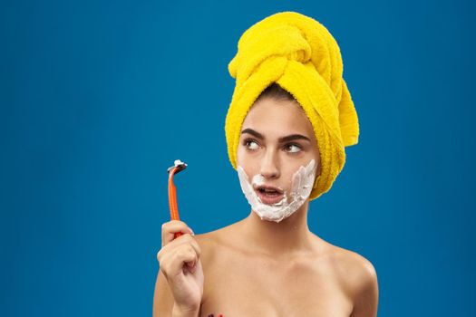 cheerful woman with a yellow towel on his head shaving blue background. High quality photo