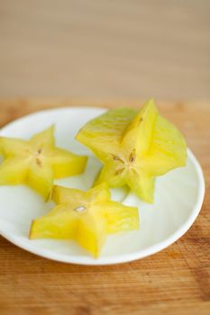 Exotic starfruit or averrhoa carambola on white plate on wooden cut board. Healthy food, fresh organic star apple fruit