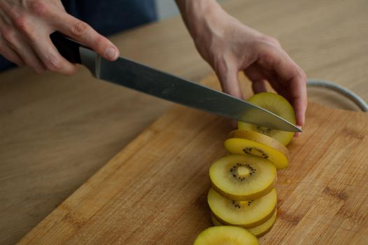 Female hands is cutting a fresh ripe golden kiwi fruit on a cut wooden board. Exotic fruits, healthy eating concept.