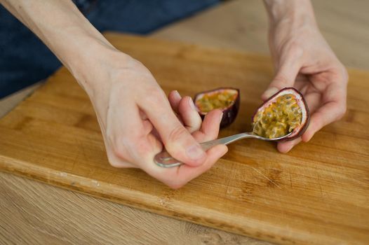 Female eats fresh organic ripe granadilla or yellow passion fruit with a spoon. Exotic fruits, healthy eating concept.