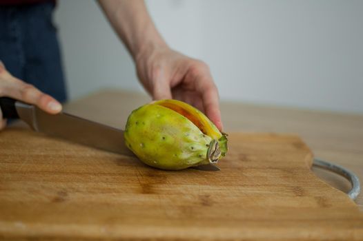 Female hands is cutting a fresh ripe cactus pear on a cut wooden board. Exotic fruits, healthy eating concept