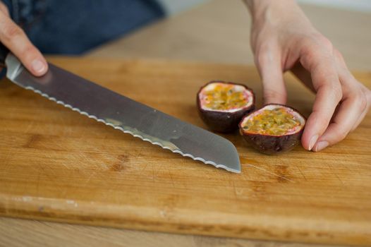 Female hands is cutting a fresh ripe passion fruit, maracuya on a cut wooden board. Exotic fruits, healthy eating concept.