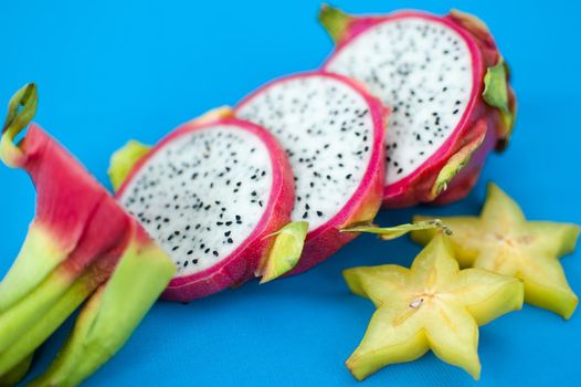 Slices of dragon fruit or pitaya with pink skin and white pulp with black seeds on blue background. Exotic fruits, healthy eating concept.