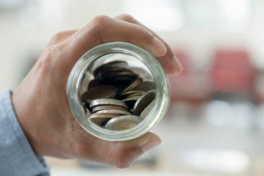 Businessman saving money concept. Hand holding coins putting in jug glass