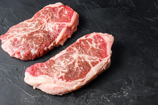Organic top blade steak cuts, on black textured background side view with space for text