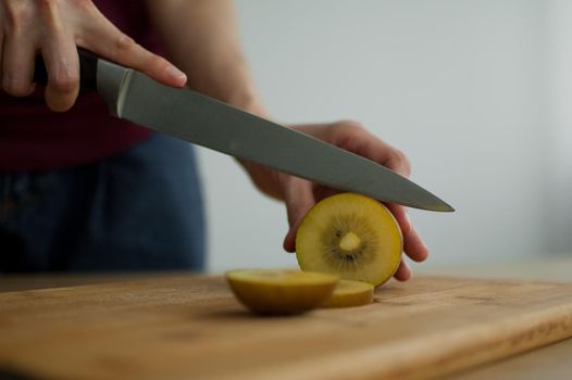 Female hands is cutting a fresh ripe golden kiwi fruit on a cut wooden board. Exotic fruits, healthy eating concept.