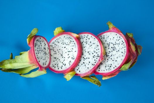 Slices of dragon fruit or pitaya with pink skin and white pulp with black seeds on blue background. Exotic fruits, healthy eating concept.
